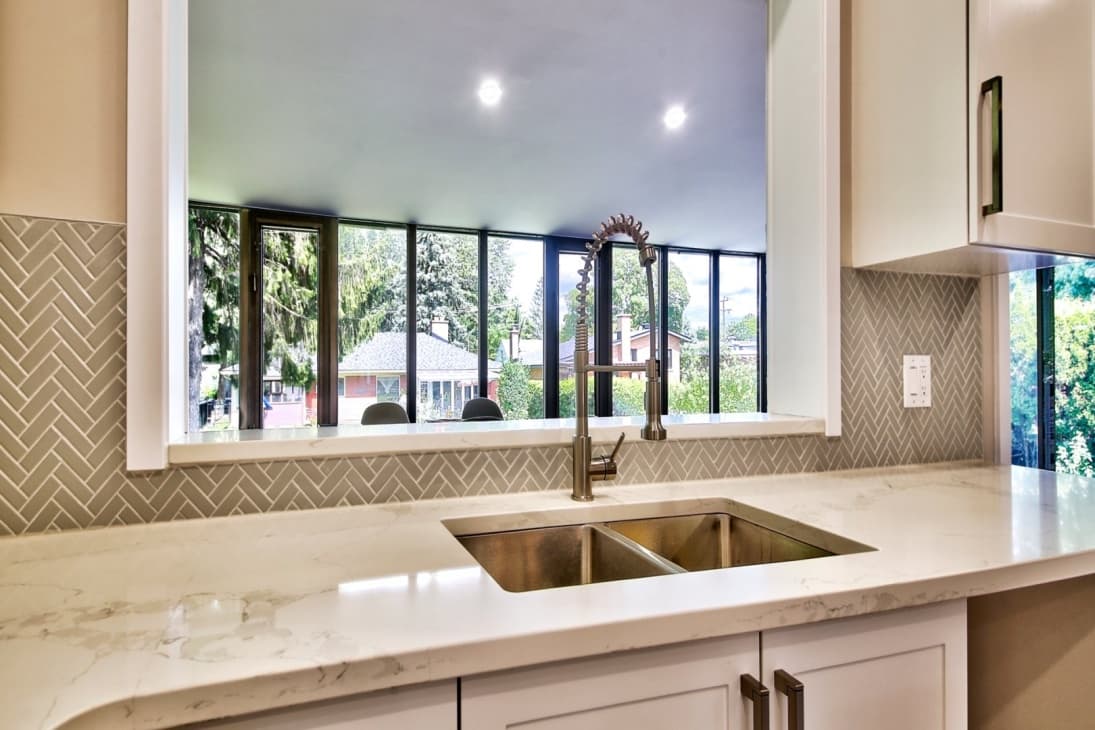 White quartz sink detail with herringbone tile backsplash and panoramic windows